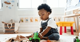 Young child playing with wooden toys on the floor in a bright playroom with colorful decorations.
